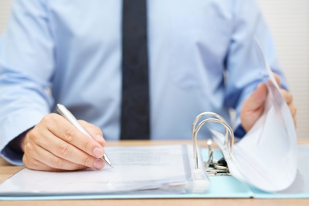 A man in a blue shirt is holding a pen at a desk.