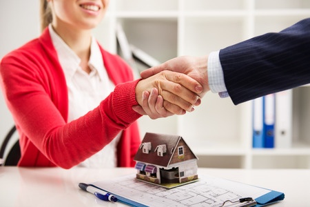 A man and woman shaking hands in front of a house model.