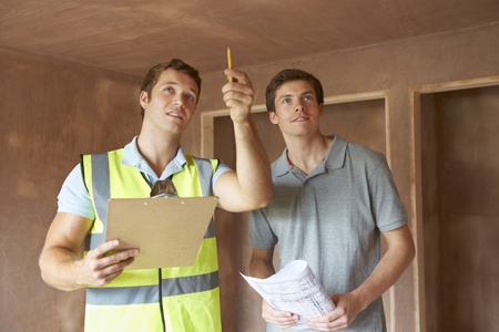 Two construction workers standing in a room with a clipboard.