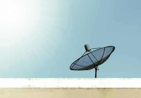 A satellite dish on top of a wall with the sun behind it.