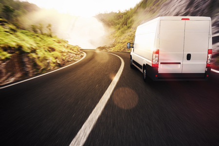 A white van is driving down a mountain road.