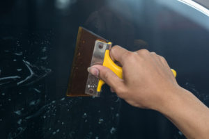 A person is using a yellow sponge to clean a car windshield.