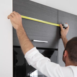 A man using a measuring tape to measure the door of a kitchen.