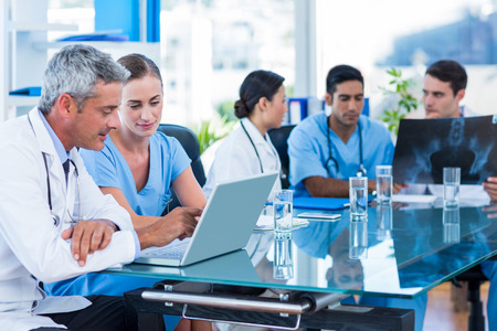 A group of doctors sitting around a table with laptops.