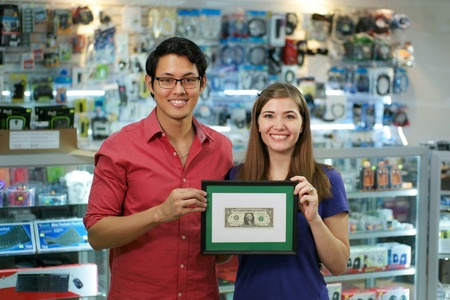 A man and woman holding a framed dollar bill in a store.