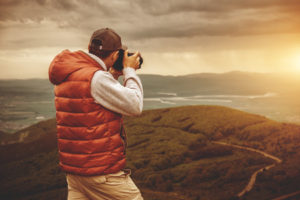 A man is taking a picture of a mountain at sunset.