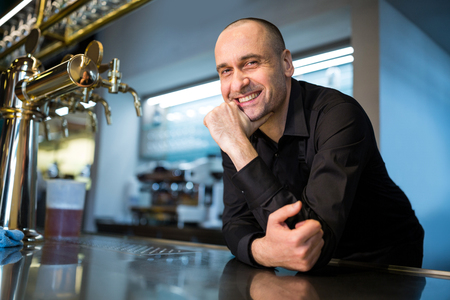 A man leaning over a bar with a beer tap.