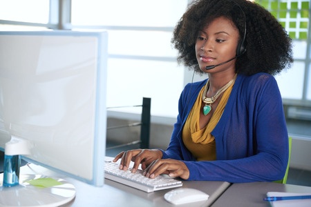 A woman wearing a headset is working on a computer.