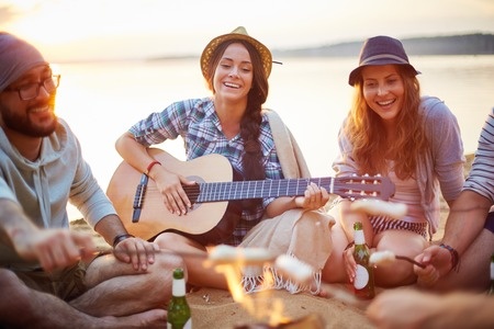 A group of friends sitting around a campfire and playing guitar.