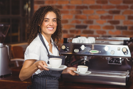 A smiling barista holding a cup of coffee in front of a coffee machine.