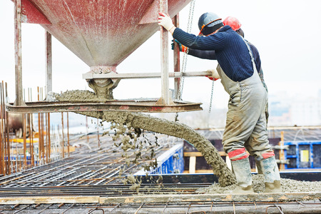 A construction worker pouring cement into a concrete mixer.