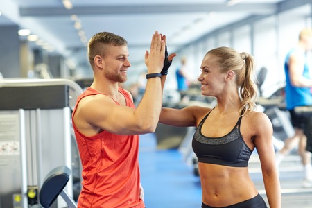 A man and woman giving each other a high five in a gym.