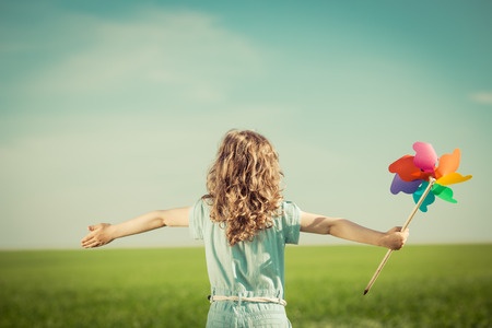 A little girl is standing in a field with a colorful pinwheel.