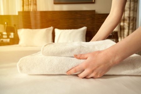 A woman is putting towels on a bed in a hotel.