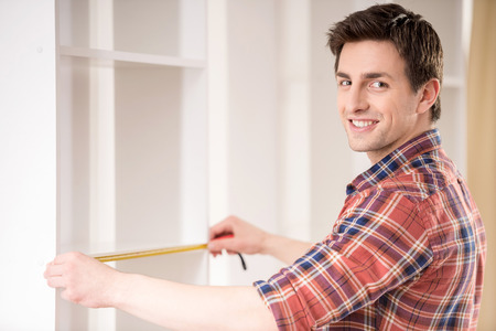 A man is holding a measuring tape in front of a wall.