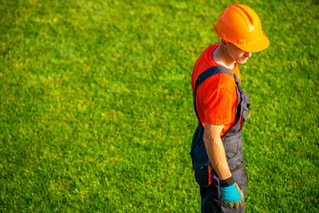 A construction worker is standing on a green field.