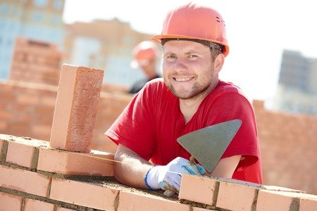 A man in a hard hat is laying bricks on a construction site.