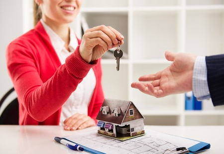 A woman handing a key to a model house to a man.