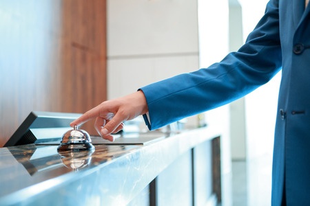 A man in a blue suit is pointing at a bell at a hotel.