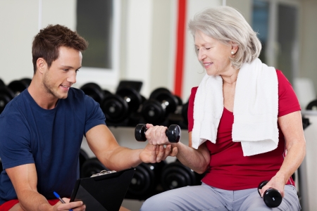 A woman is helping an older woman with dumbbells in a gym.