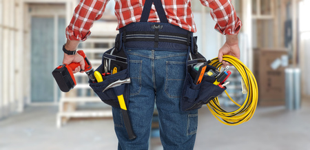 A man with a tool belt and tools is standing in front of a building.