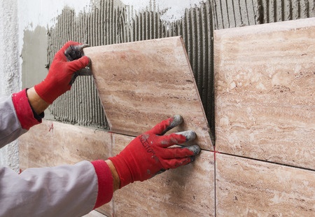 A worker is laying tiles on a wall.